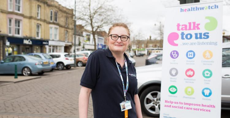 Female volunteer standing in front of a Healthwatch banner 