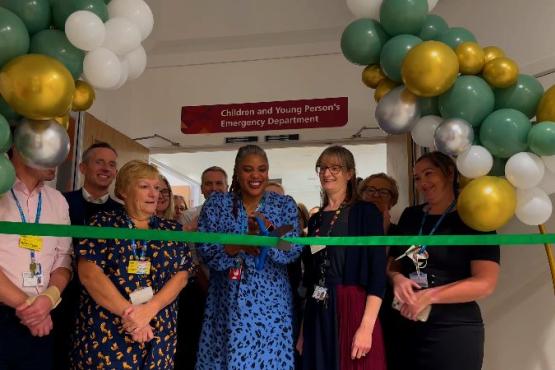 North West London employees are standing in a group behind a green ribbon. There is a lady in a blue address who has scissors to cut the ribbon.