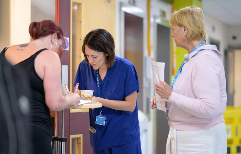 Three women in a hallway filling out a form. Two are clinicians.